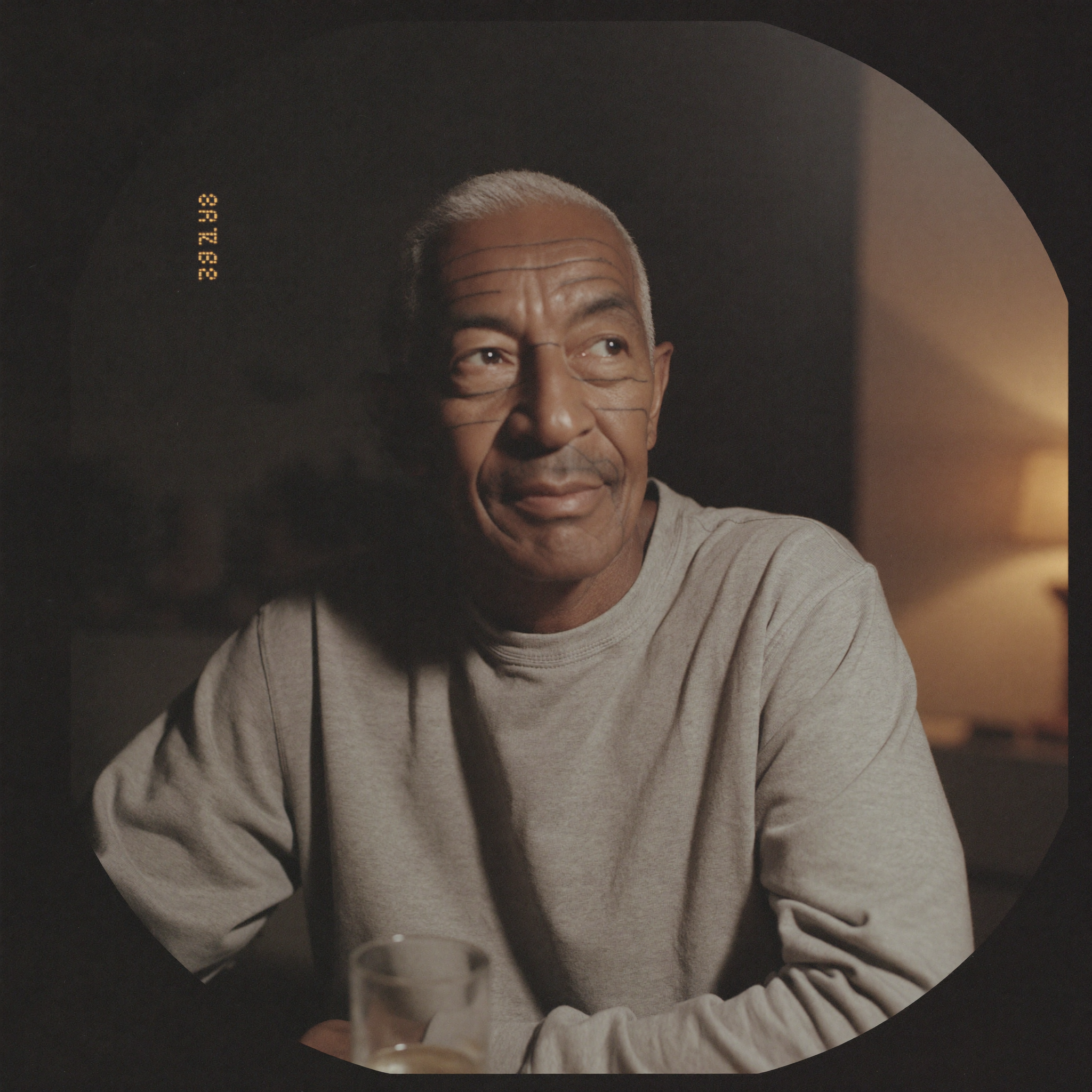 A man in his early sixties sitting at a kitchen table in the evening with a glass of water